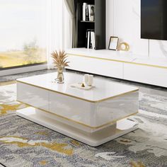 a white coffee table with gold accents in front of a large window and a television on the wall