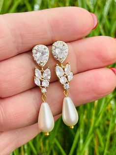 a pair of white pearls and gold earrings on someone's hand with grass in the background