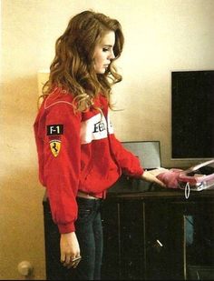 a woman in a red jacket standing next to a tv and holding a remote control