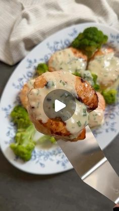 a person is holding a knife over some food on a white and blue plate with broccoli