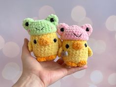 two small crocheted toy animals are held in their hands, one is yellow and the other is pink