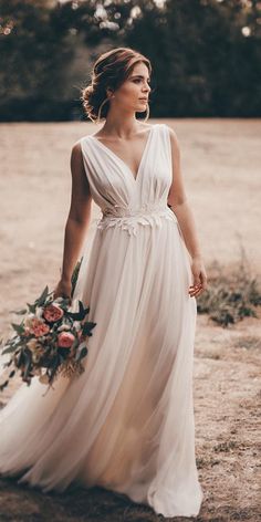 a woman in a white dress is holding a bouquet and looking off into the distance