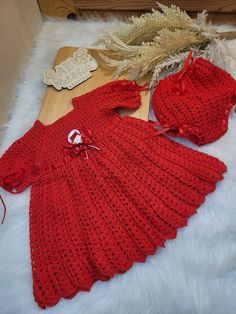 a red knitted dress and matching hat are laying on a white furnishing