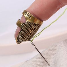 a hand holding a gold ring with a needle in it and thread on the tip