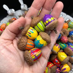 a hand is holding some fake pine cones and acorns that are decorated with colorful designs