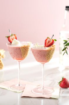 two glasses filled with dessert and strawberries on top of a table next to a bottle