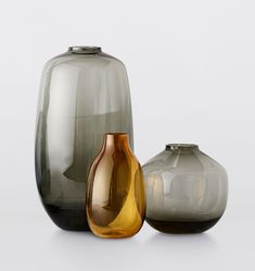 three different colored vases sitting next to each other on a white surface with no one around them