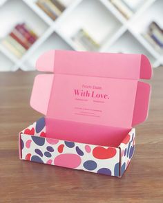 an open pink box sitting on top of a wooden table next to a book shelf