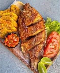 fish and vegetables on a cutting board with limes, tomatoes, and sauces