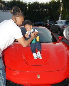 a man holding a small child in front of a red sports car