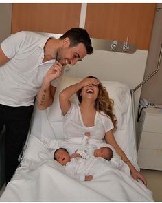 a man standing next to a woman in a hospital bed with two babies on her lap