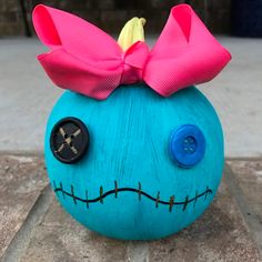 a blue pumpkin with a pink bow on it's head sitting on the ground