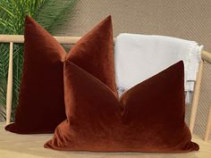 two brown pillows sitting on top of a wooden chair next to a white towel and potted plant