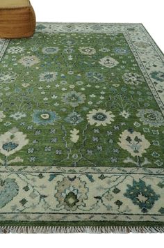 a green rug with blue and white flowers on the ground next to a wooden bench