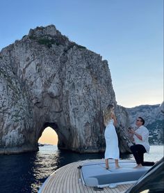 a man and woman standing on the bow of a boat in front of a rock formation