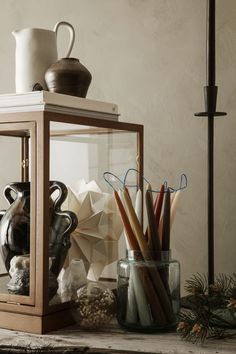 a glass case with pencils and other items in it sitting on a table next to a lamp