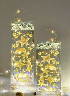 two clear glass vases with gold stars and moon lights in them on a white surface