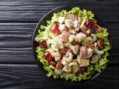 a salad with chicken, grapes and lettuce on a black plate