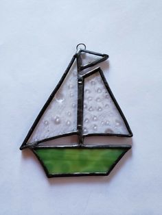 a stained glass sailboat ornament hanging on a white wall with water droplets