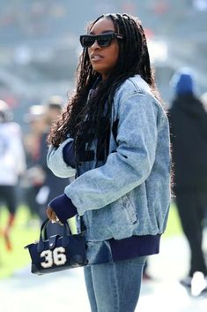 a woman with long hair wearing sunglasses and holding a handbag in her right hand