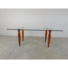 a glass table with two wooden legs on the top and one leg bent down, in front of a white wall