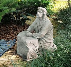 a statue of jesus sitting on top of a rock in the middle of a garden