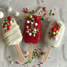 three popsicles decorated with christmas decorations and sprinkles are on a white surface