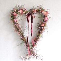 a heart shaped wreath with pink flowers and greenery hanging from the side on a white wall