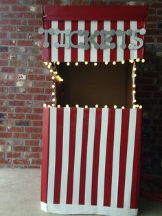 a red and white striped ticket booth with lights on the top, in front of a brick wall