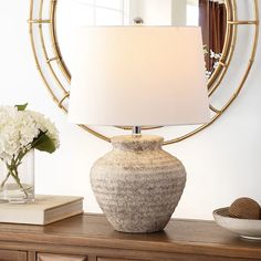 a table lamp sitting on top of a wooden dresser next to a vase with flowers