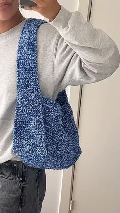 a woman holding a cell phone up to her ear while wearing a blue knitted bag