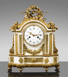 an ornate gold and white clock with cherubs on the sides, against a gray background