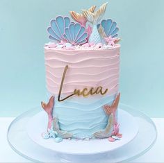 a pink and blue cake with mermaid decorations on it's top, sitting on a plate