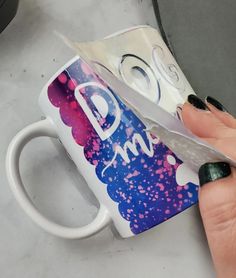 a person holding a pair of scissors in front of a coffee mug with the word dm on it