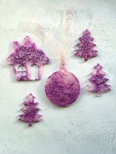 purple ornaments are arranged on a white surface with trees in the center and a house shaped ornament hanging from it