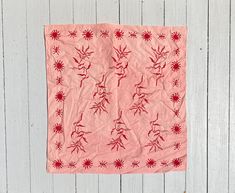 a piece of cloth with red flowers on it hanging from a white wooden wall next to a pair of scissors