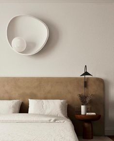 a bed with white sheets and pillows next to a wall mounted round object on the wall