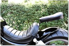 a black motorcycle seat sitting on the back of it's seat in front of some bushes