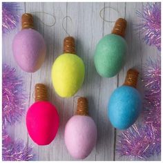 four different colored ornaments hanging from strings on a white table with tinsel and purple tinsel