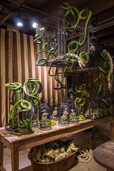 a table topped with lots of cages filled with green snake figurines and birds