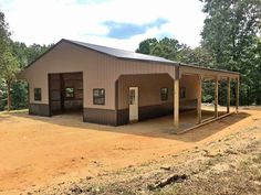 a large metal building sitting in the middle of a dirt field next to some trees