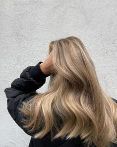 a woman with long blonde hair standing in front of a white wall wearing a black jacket