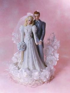 a bride and groom figurine standing next to each other on a pink background