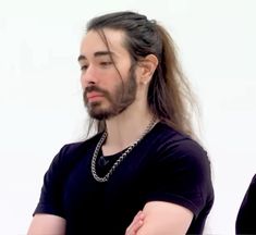 a man with long hair wearing a black t - shirt and silver chain around his neck