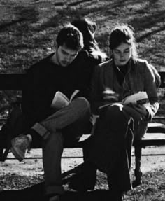 two people are sitting on a bench and one is looking at a book while the other looks down