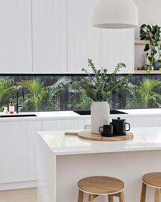 a kitchen with two stools next to a counter top and potted plants on the window sill