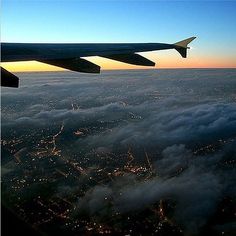 an airplane wing flying over the city lights at night in the sky above the clouds