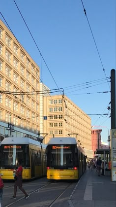 two yellow and white trains parked next to each other on the tracks in front of tall buildings