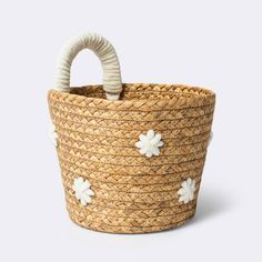 a woven basket with white flowers on the handle and handles, sitting in front of a gray background