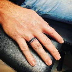 a man's hand with a wedding ring on his left finger, resting on a black leather chair